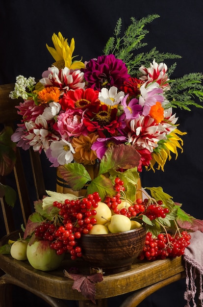 Herfst sfeerstilleven met een kleurrijk mooi boeket tuinbloemen, rode bessen, appels, herfstbladeren op een zwarte ondergrond.