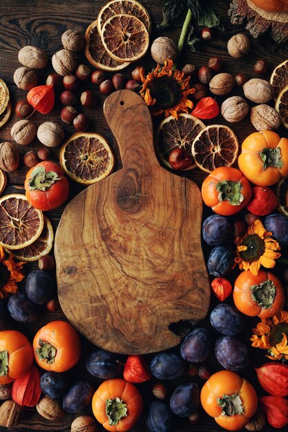 Herfst stilleven compositie met fruit en groenten assortiment van pruimen persimmon walnoot zonnebloemen en droge sinaasappels en rustieke houten plank bovenaanzicht ruimte voor tekst