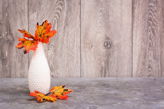 Herfst stilleven. Een vaas met oranje esdoornbladeren op de tafel. Wit-oranje-beige kleurenschema. Kopieer ruimte