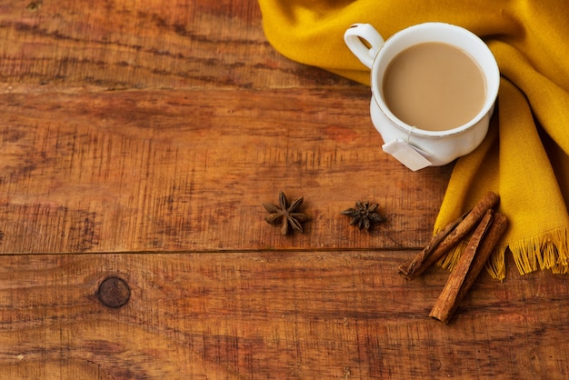 Herfst thee kopje samenstelling met melk, gele sjaals, kaneelstokjes op een houten achtergrond. Herfst achtergrond. Warme, gezellige sfeer van de herfst. Plat leggen, lay-out. Plaats voor tekst, frame