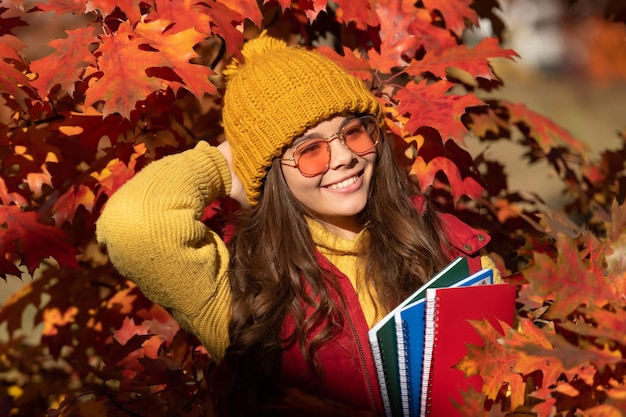 Herfst tiener meisje portret in herfst herfstbladeren glimlachend kind houd werkmap op herfstbladeren achtergrond