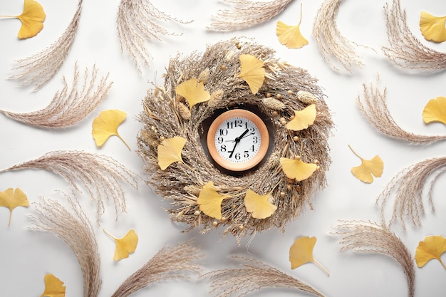 Herfst tijd achtergrond houten wekker in droog gras krans van witte plat lag herfst achtergrond met ginko bladeren en pampas gras