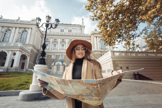 Herfst toerisme. Jonge aantrekkelijke vrouwelijke reiziger wordt geleid door de stadsplattegrond. Mooi meisje op zoek naar richting in de Europese stad. Vakantie en toerisme concept