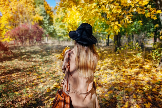 Herfst vibes. Jonge vrouw die in de herfstbos loopt onder dalende bladeren. Stijlvolle meisje met hoed