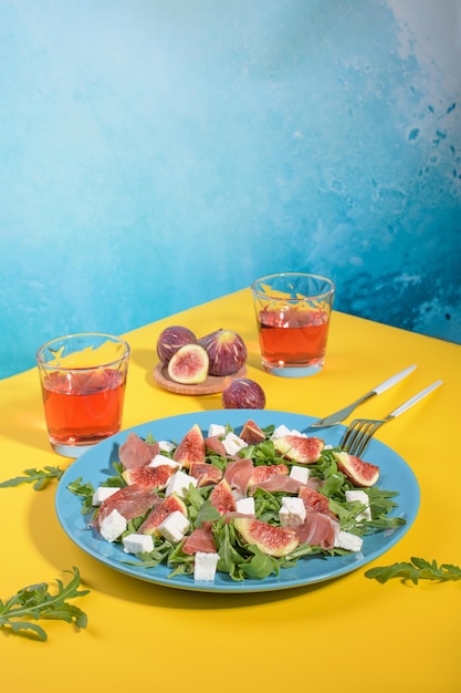 Herfst vijgensalade met rucola feta rauwe ham in blauwe plaat op gele en blauwe achtergrond geserveerd met rose wijn