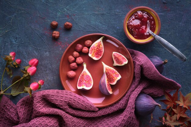 Herfstachtergrond met vers gehalveerd vijgenfruit op terracotta keramische plaat Magenta handdoek en rode esdoorn Herfstbladeren op donkerpaars bord Vijgenjam in keramische kom