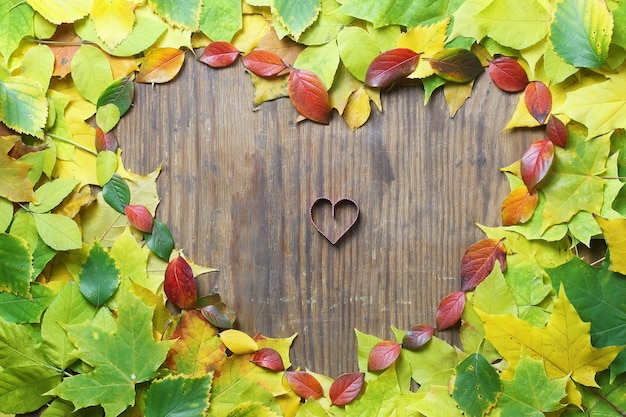 Herfstbladeren achtergrond in vorm van hart op houten tafel