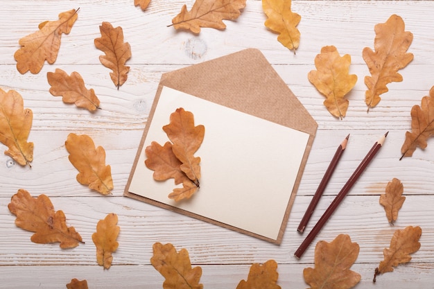 Herfstbladeren en envelop op een witte houten tafel