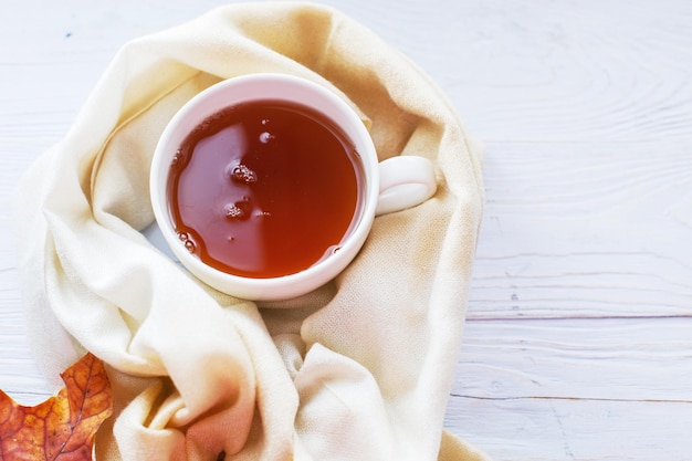 Herfstbladeren met een kopje thee of koffie naast een sjaal op een houten ondergrond met kopieerruimte