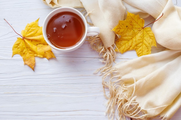 Herfstbladeren met een kopje thee of koffie naast een sjaal op een houten ondergrond met kopieerruimte