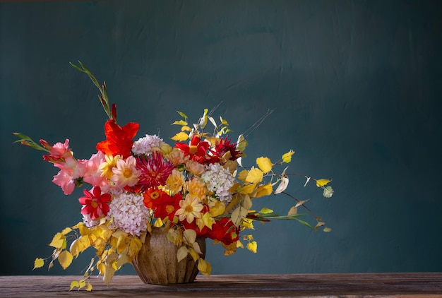 Herfstboeket met rode en gele bloemen in keramische vaas op donkere achtergrond