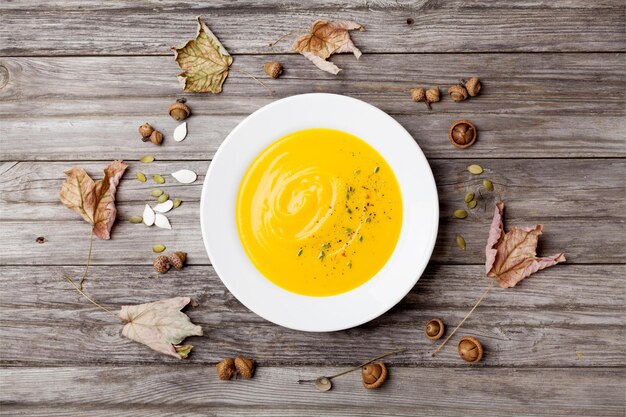 Herfstgroenten- of pompoensoep in een witte kom op een houten rustieke tafel.