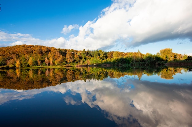 Herfstlandschap kleurrijke bomen spiegelen in het water van het meer Witte pluizige wolken bloeien veelkleurig herfstbos Rustige natuurlijke schoonheid