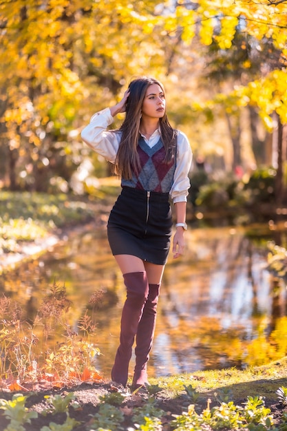 Herfstlevensstijl, een jonge blanke brunette, studente in een modieuze pose, in een park aan een meer
