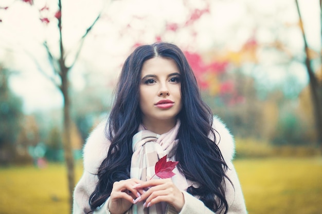 Herfstmeisje dat autdoors droomt met rode esdoornbladeren Jonge vrouw met lang golvend haar in herfstpark