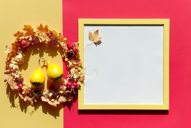 Herfstmodel met copyspace in vierkant frame Gedroogde bloemenkrans met droge herfstbladeren en bessen op rode en gele papieren achtergrond Direct zonlicht met schaduwen