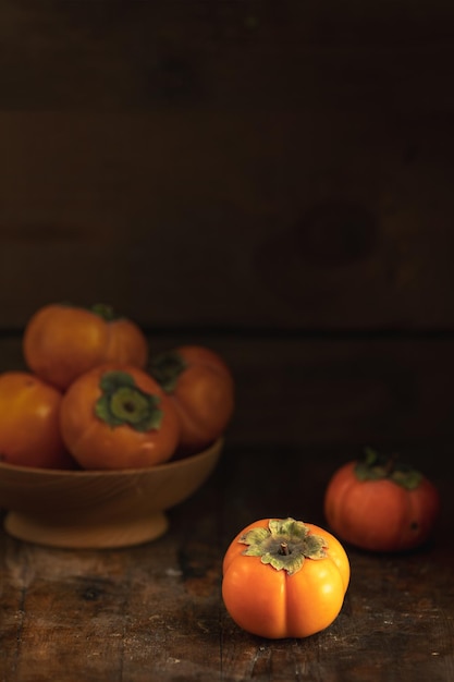 Herfstoogst Persimmon-vruchten in kom op een houten tafelachtergrond Kopieer ruimte Donkere rustieke stijl Natuurlijke remedie