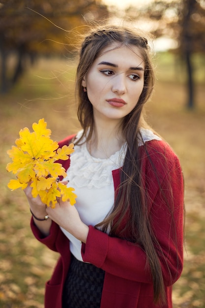 Herfstportret van een meisje in het park in een bordeauxrood vest.