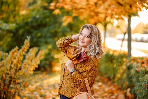 Herfstportret van een meisje met een grote maat met een boeket gele bladeren in haar handen Stijlvolle vrouw in het herfstpark