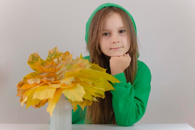 Herfstportret van een mooi gelukkig babymeisje met lang haar in een groene trui die poseert met gele bladeren Herfststemming