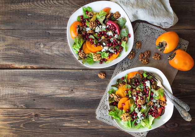 herfstsalade met kaki granaatappel blauwe kaas en walnoten op rustieke houten achtergrond