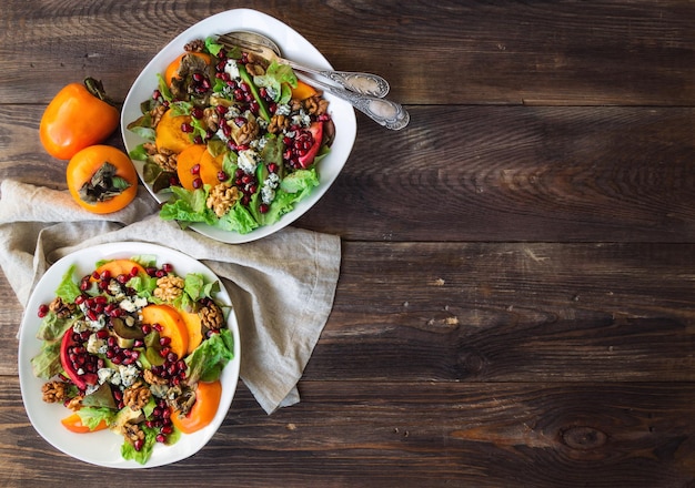 Herfstsalade met kaki granaatappel blauwe kaas en walnoten op rustieke houten achtergrond