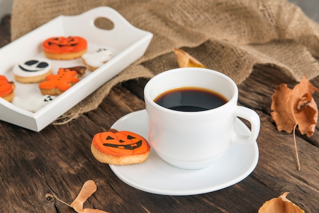 Herfstsamenstelling van oranje en witte koekjes voor Halloween, kopjes geurige zwarte koffie staat op bruin houten tafel