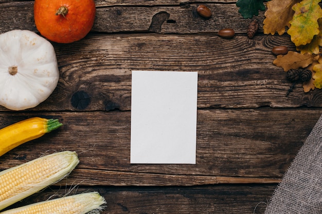 Herfststemming: witte lege huidige kaart, pompoenen en maïs met gele bladeren op hout