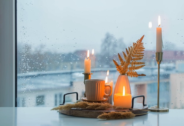 Herfststilleven met brandende kaarsen en een kopje koffie op de achtergrond van een raam met regendruppels