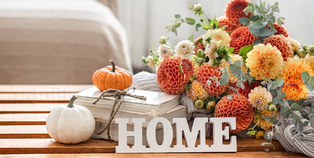 Herfststilleven met een boeket chrysantenbloemen, het decoratieve woord huis en pompoenen op een onscherpe achtergrond.