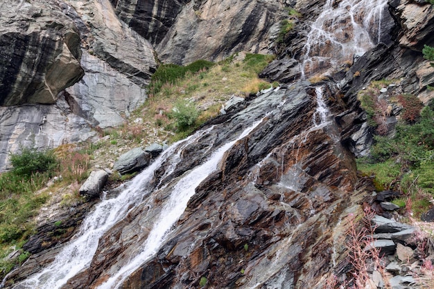 Herfstvegetatie van mossen en kruiden op bruine karst granietrotsen gewassen door een alpine waterval