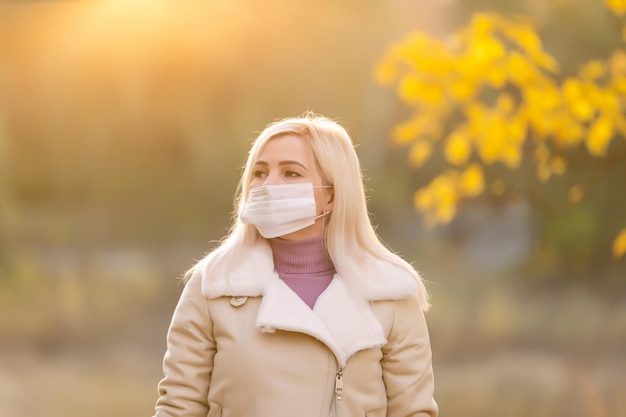 Herfstvrouw met medisch beschermend gezichtsmasker die buiten loopt, herfstseizoenportret