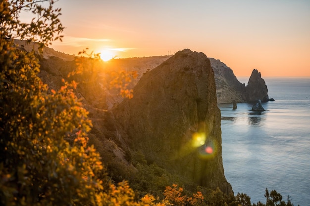 Herfstzeelandschap met warm zonsonderganglicht over rotsachtige kustlijn kalme zee op een achtergrond van rotsachtig