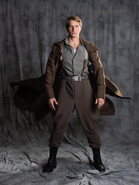 Photo hero in a military style with a gun in his hands a young man in a long brown coat and breeches with