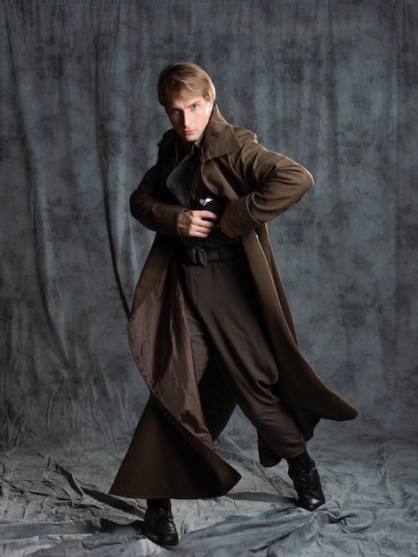 Hero in a military style with a gun in his hands a young man in a long brown coat and breeches with