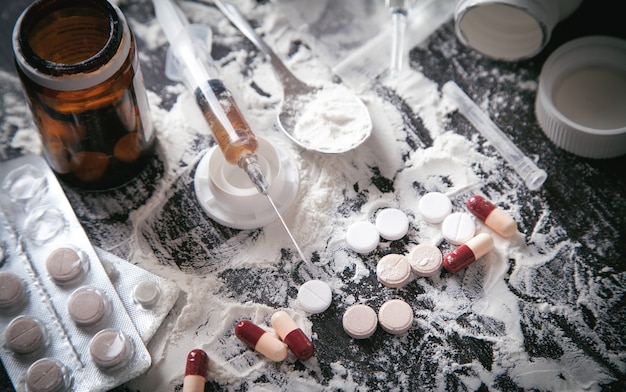 Фото Порошок героина, таблетки и шприц на темном фоне.