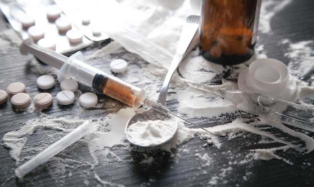 Heroïnepoeder, pillen en spuit op de donkere achtergrond.