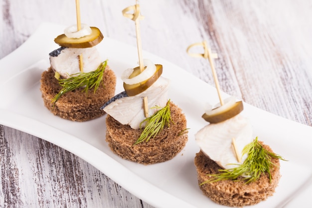 Photo herring canape with onion, pickled cucumber and dill