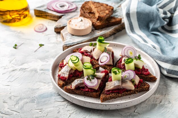 Herring fillet Scandinavian cuisine sandwich with slices of pickled Atlantic herring fillet beetroot salad green cucumber onion and microgreen