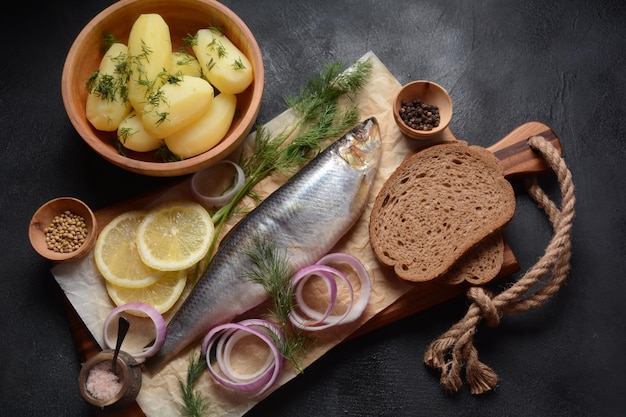 Herring fish  on wooden board  with pepper herbs red onion and lemon on black  background