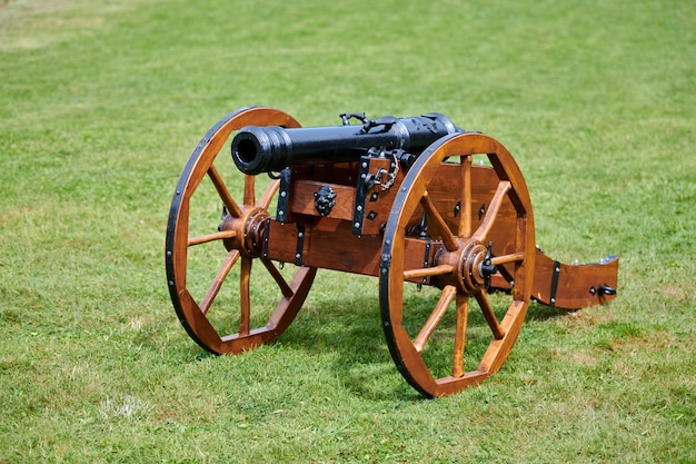 Hersteld kanonmodel voor kasteeldefensie, groene gazonachtergrond. Artillerie groot kaliber kanon, oud oud kanon op houten wielen. Bescherm tegen vijandelijke aanvallen, historische re-enactment van de burgeroorlog;