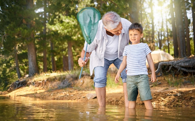 Hes always ever ready for an adventure. Shot of a little boy and his grandfather fishing with a net at at lake in a forest.