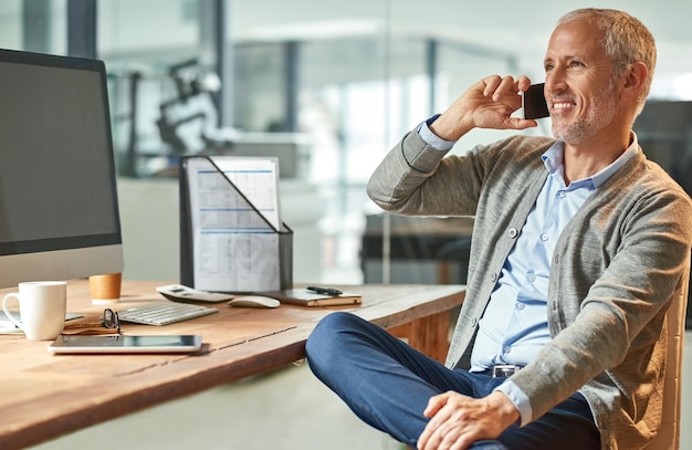 Hes great with clients Shot of a mature businessman talking on the phone while sitting at his desk in an office