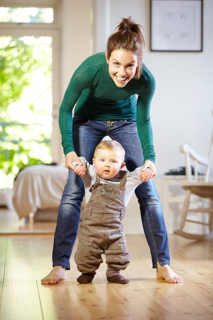 그는 너무 빨리 배우고 있습니다. 그녀의 아기가 걷는 법을 배우는 것을 돕는 웃는 젊은 엄마