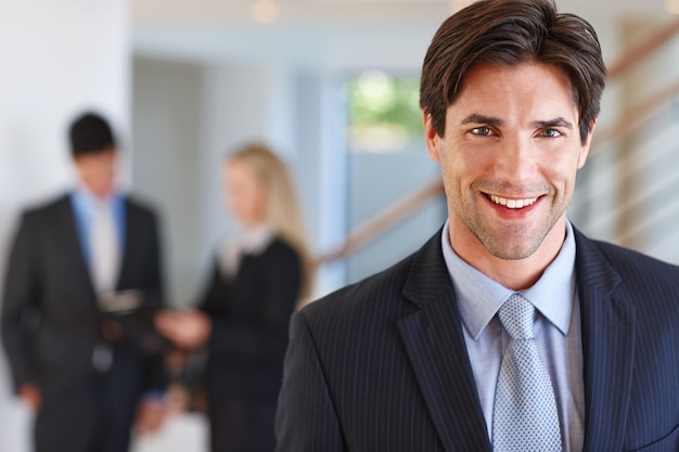 Hes one of the best in his field Portrait of a businessman standing indoors with two colleagues in the background