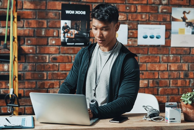 Hes receiving even more subscriptions online Cropped shot of a handsome young male fitness instructor using a laptop while working in a gym