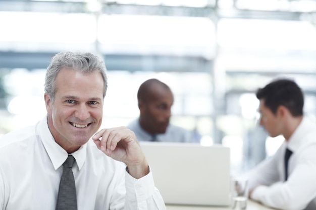 Hes a well balanced employer Portrait of a mature businessman smiling while sitting in front of two younger colleagues