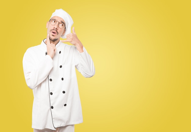 Hesitant young chef making a gesture of calling with the hand