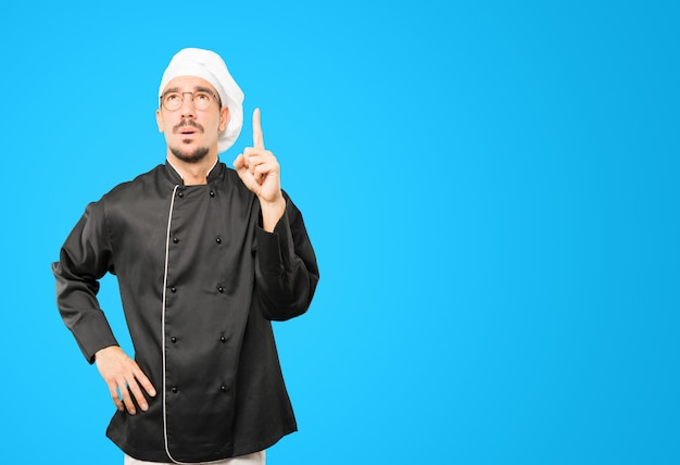 Hesitant young chef pointing up with his finger