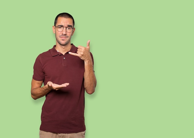 Hesitant young man making a gesture of calling with the hand